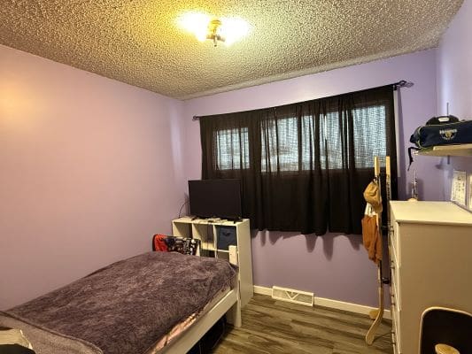 Purple bedroom with bed, dresser, and window.