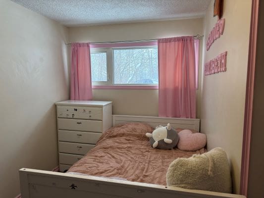 Bedroom with pink curtains and stuffed toys.