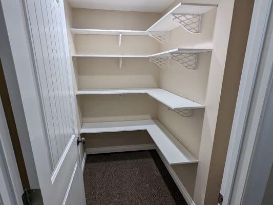 Empty pantry with white corner shelves.