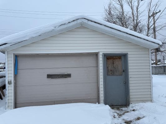 Snow-covered garage with boarded-up door.
