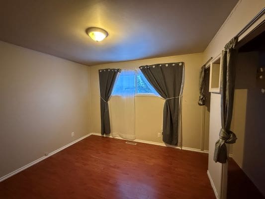 Empty room with wooden floor and curtains.