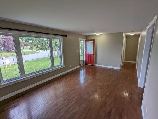 Empty living room with wooden floor and windows.