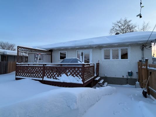 Snow-covered house with wooden deck.