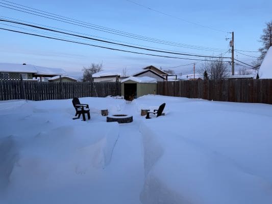 Snowy backyard with chairs and fire pit.