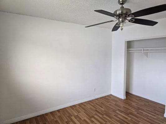 Empty room with wooden floor and fan.