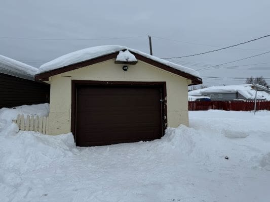 Snow-covered garage with brown door.