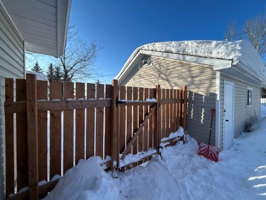 Snow-covered fence and shed in winter.