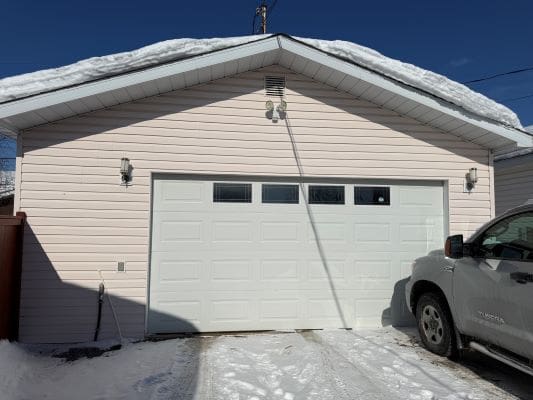 Garage with snow-covered roof and driveway.