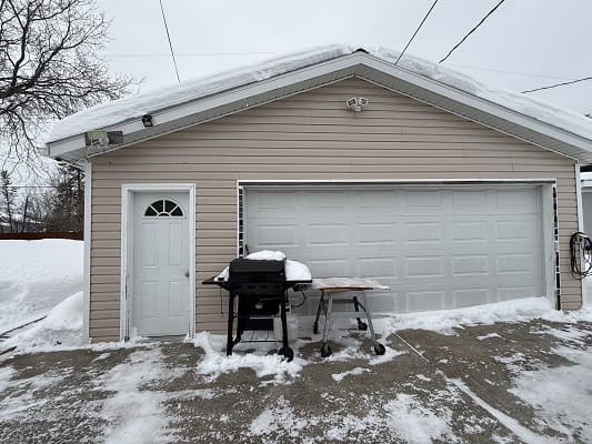 Snow-covered garage with barbecue grill outside.