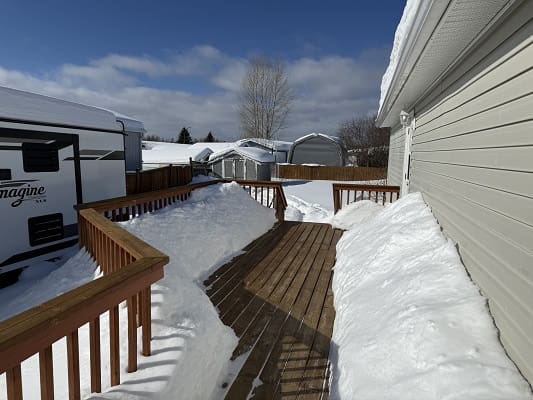 Snow-covered deck and parked RV in winter.
