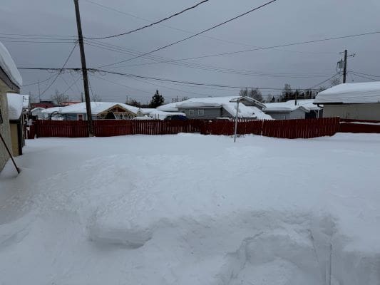 Snow-covered backyard with red fence.