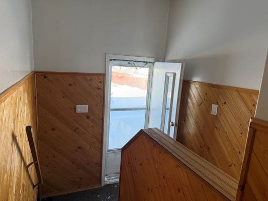 Staircase with wooden walls and open door.