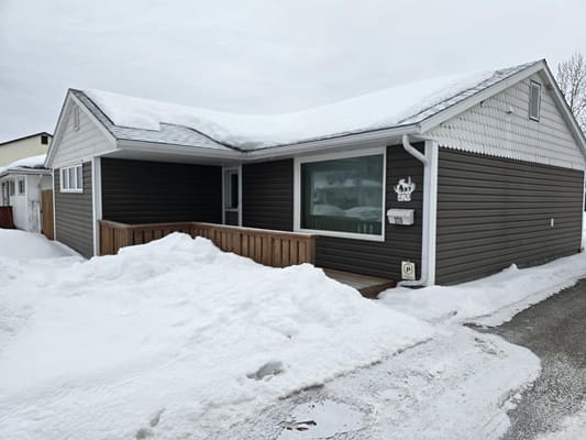 Snow-covered house with dark siding exterior.
