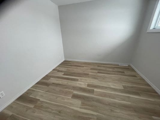 Empty room with wooden flooring and window.
