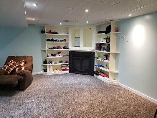 Basement room with shelves and fireplace.