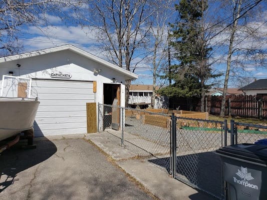 White garage with fenced yard and trees.