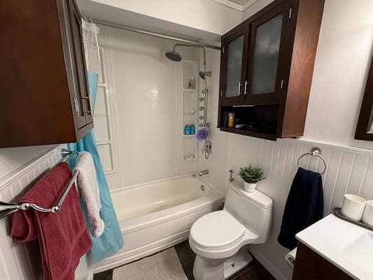Small bathroom with bathtub and wooden cabinets.