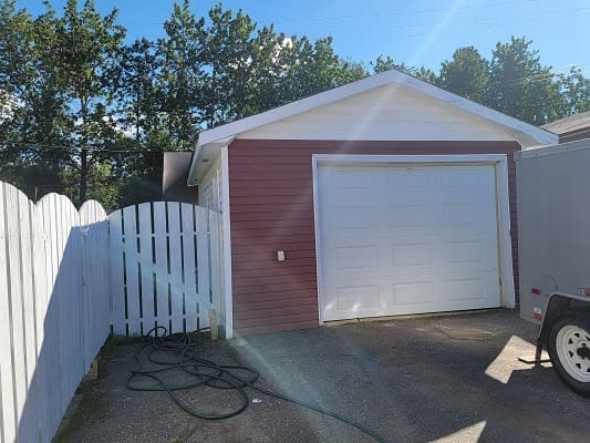 Red garage with white fence and hose.